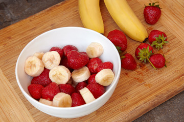 Healthy meal with strawberry and bananas. Organic natural diet concept, real natural fruits, fresh and washed, in  white bowl on wooden desk. Copy space.