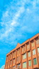 Vertical Commercial building with red brick wall viewed against blue sky and clouds