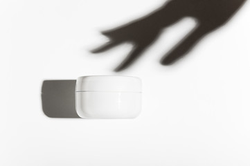 Women hand shadow touching cosmetic balm package. Facial care, skin moisturizer unbranded bottle mockup. Hand cream, hair lotion blank jar on white background. Plastic container for skincare product