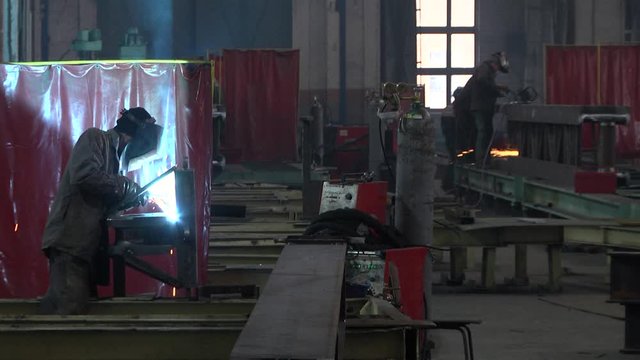 Workers weld metal structures at the factory. Welders use electric welding machines.