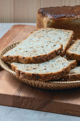slices of grain bread in a basket and a loaf of wheat  bread on the kitchen table