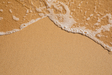 Waves breaking on an empty sand beach and spalsh producing foam - travel holiday vacation summer sun - splashing water - wavy golden yellow sand background - empty space