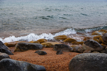 Stones on the sea beach. Pasture winter day. Clear water and sand. Kyrgyzstan, Issyk-Kul Lake