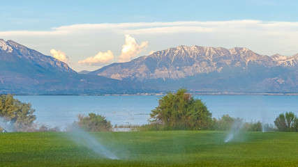 Pano frame Water from sprinklers on a green grassy land with scenic nature background