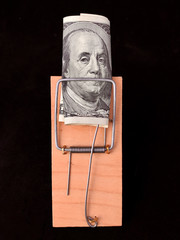 Dollars in a mousetrap on a black background. Wooden trap with bait and mechanism for rats and mice. Concept: happiness is not money, greed