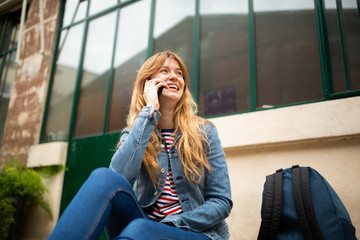 happy young woman sitting outside talking with cellphone