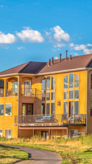 Vertical Road amidst grassy land in front of beautiful homes against blue sky with clouds