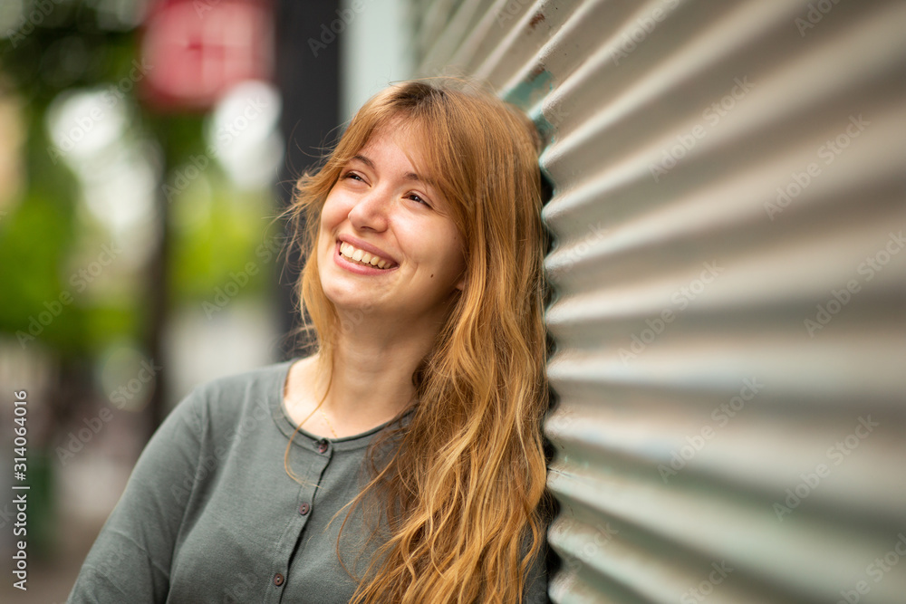 Wall mural close up smiling young woman leaning against wall and looking away