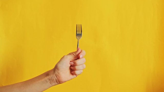 Fork in female hand with cauliflower on yellow background. Healthy food, vegan concept
