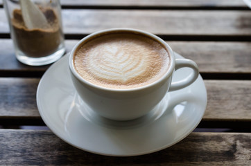 A cup of coffee with heart pattern in a white cup on wooden background