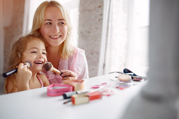 Family sitting infront a mirror. Mother in a pink pajamas. Little girl with cosmetics.