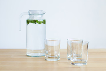 carafe with water and mint and several glass glasses on a wooden table with a light background