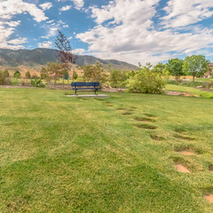 Square Grassy lawn with stone steps and blue bench gainst mountain and cloudy blue sky