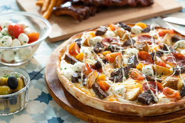 Pan pizza with grilled meat, potato, tomatoes and vegetables with pickles and side dish.