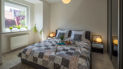 Modern interior of bedroom. Tray with food on the bed. Bedsides with round lamps. Window.