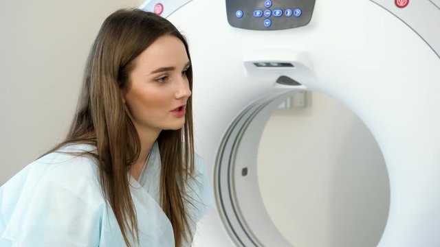 Closeup of young adult female patient talking to doctor during CT or MRI scan procedure. Beautiful smiling woman on a medical examination. 4K