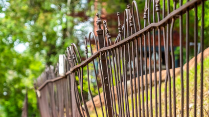Pano frame Close up of old and rusty iron fence against grassy slope ground and lush trees