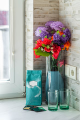 Couple of green glasses. Glass vase with purple, pink and orange flowers.