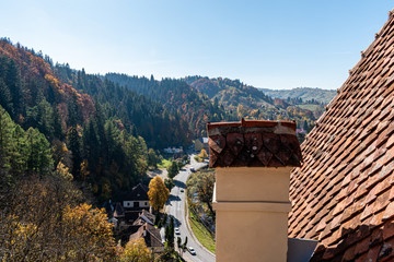 the roof of an old building in Romania with mountains and forest blurred in the back and a clear sky. the building is on the left of the screen and on the right is free space for your text