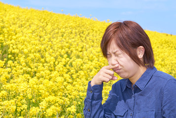 菜の花畑で鼻水を押さえる女性