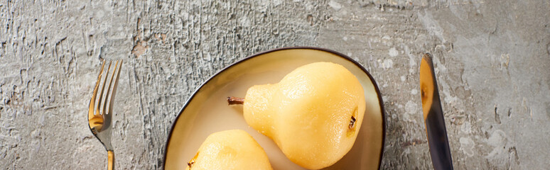 top view of delicious pear in wine served on plate near fork and knife on grey concrete surface,...