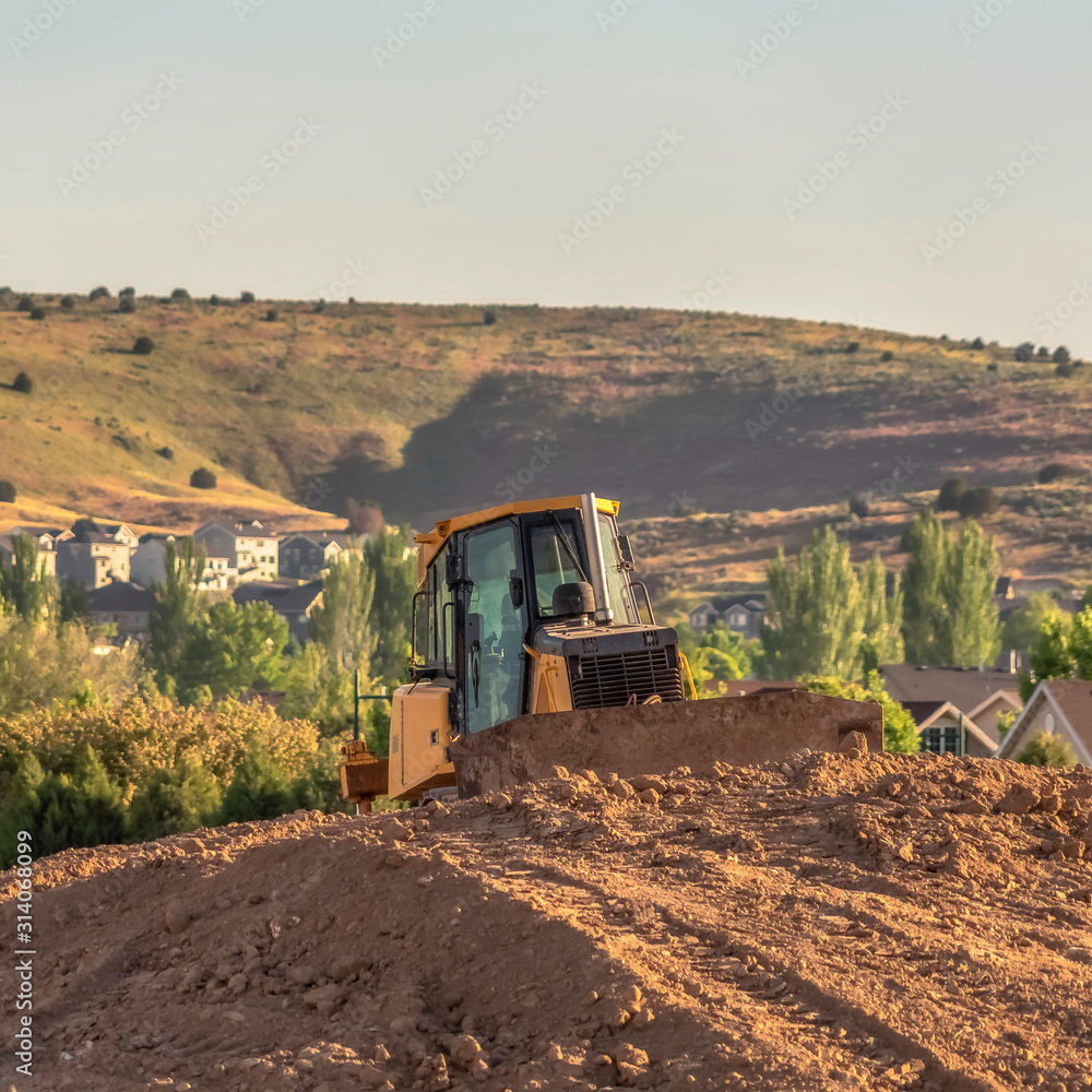 Canvas Prints Square frame Bulldozer on a mound of soil at a construction site against mountain and sky