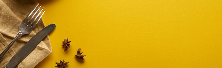 top view of anise near cutlery on beige napkin on yellow background, panoramic shot