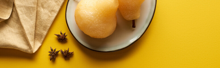 top view of delicious pear in wine with anise on plate near napkin on yellow background, panoramic shot