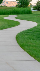 Fototapeta premium Vertical Narrow paved pathway winding through lush green grasses of park with playground