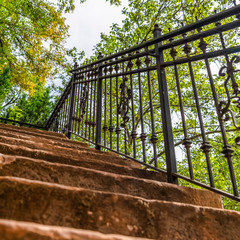 Square Close up of staircase with stone treads and metal railing against leaves and sky