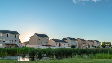 Fototapeta na wymiar Pano frame Sunset in the suburbs with multi storey homes ovelookinga park with shiny pond