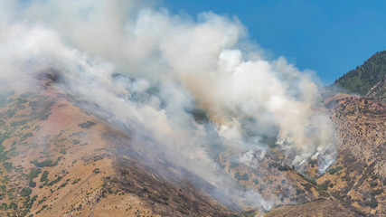 Pano frame Thick puffs of smoke from fire in the mountain against clear blue sky background