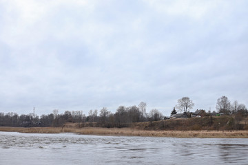 Riverside view of river flowing near countryside city with trees on winter.