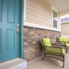 Square frame Porch armchairs against brick wall of a home with blue front door