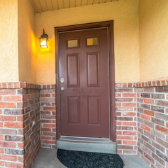 Square frame Brown door with glass panels of a home with concrete and brick exterior wall