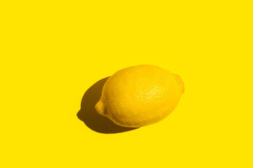 Ripe lemon on bright yellow background in bright sunlight with strong shadow. Summer fun tropical citrus fruits vitamins concept