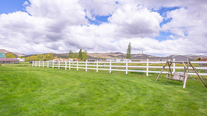 Pano Spacious yard of a home with garden swing lush green grasses and white fence