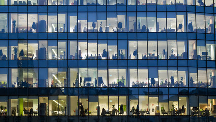 Close up view of business people working in offices from a skyscraper windows by night.