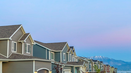 Pano frame Exterior of homes with gable and valley roofs against mountain and sky at sunset