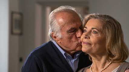 Close up of a lovely senior husband is giving a kiss to his wife as a sign of forever love at home.
