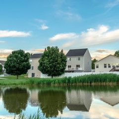 Square frame Scenic suburban landscape with homes and cloudy sky reflected on a shiny pond