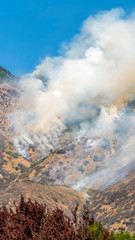 Vertical Aerial view of mountain top with vegetation and thick smoke against blue sky