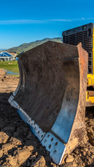 Fototapeta premium Vertical Close up of a bulldozer with metal blade yellow paint and tracks with dried mud