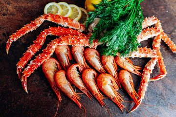 On the table are shrimp, crab, lemon and herbs. Table of reddish color.