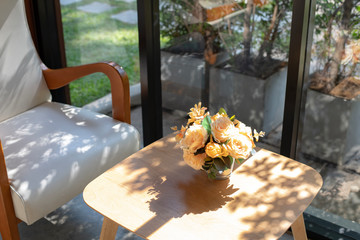 White rose vase placed on a wooden table on the side of the white chair in the glass room