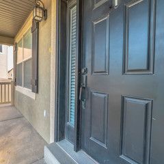 Square frame Home exterior view with gray front door sidelight and front porch on a sunny day
