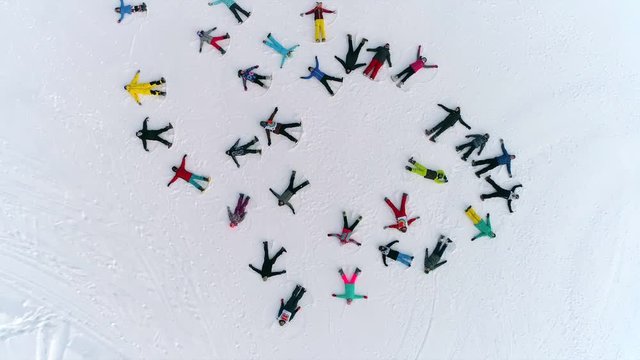 Aerial: a large group of snow angels. top view on skiers making angels in the snow and lazing in the shape of a random circle. young people in bright sports clothes represent snowangel
