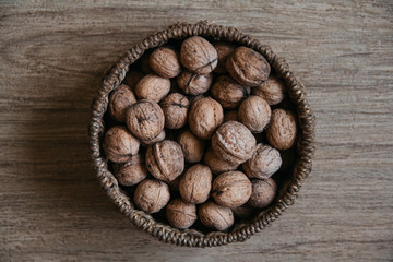 Walnuts in a round wicker basket on a wooden background. Top view. Copy, empty space for text.