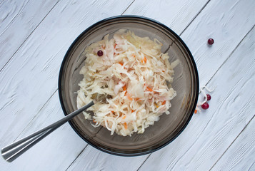 Sauerkraut in a transparent brown bowl with a fork on a white wooden table