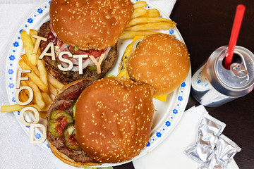 Juicy burgers and fries on a paper plate with words TASTY FOOD on burgers.